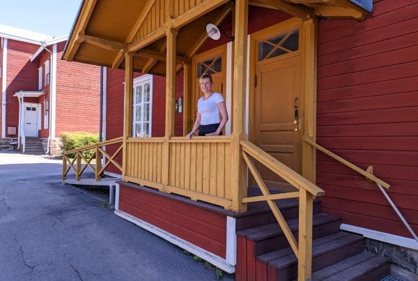 Anne Knop standing on the porch of a red and yellow wooden house on University of Vaasa campus