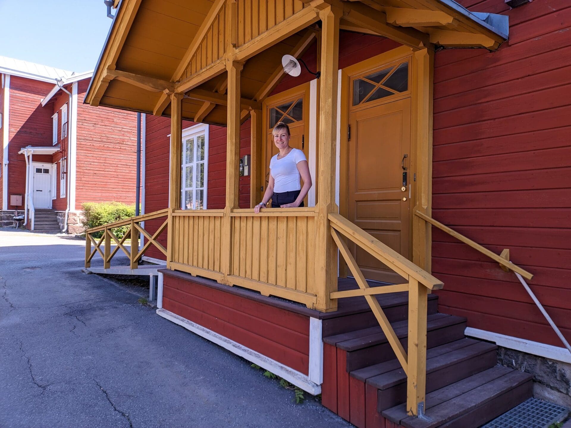 Anne Knop standing on the porch of a red and yellow wooden house on University of Vaasa campus